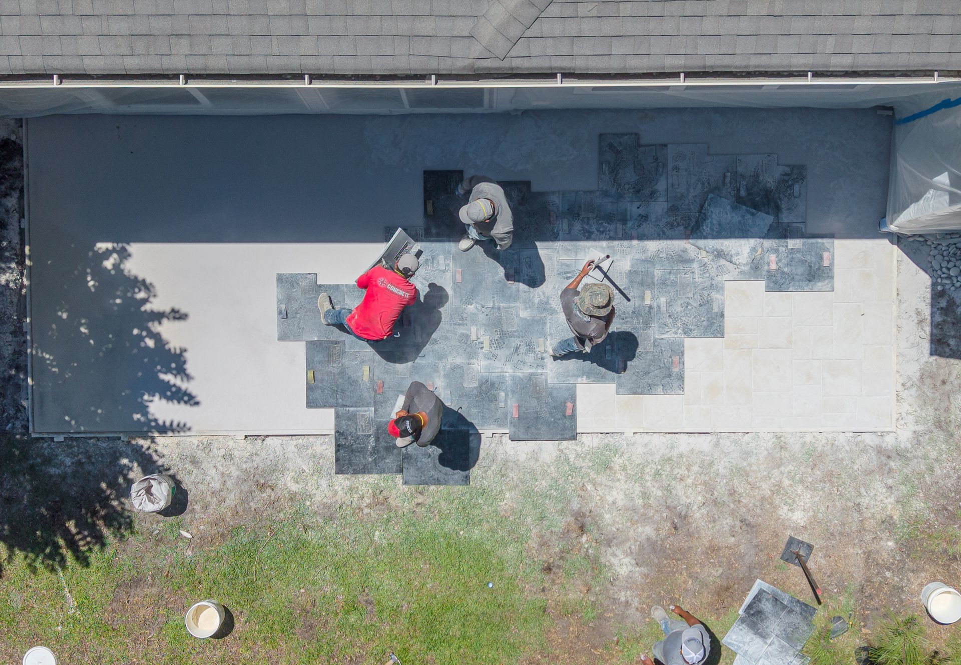 Four people on a patio by a building, including one in a bright red jacket and one holding a bag.