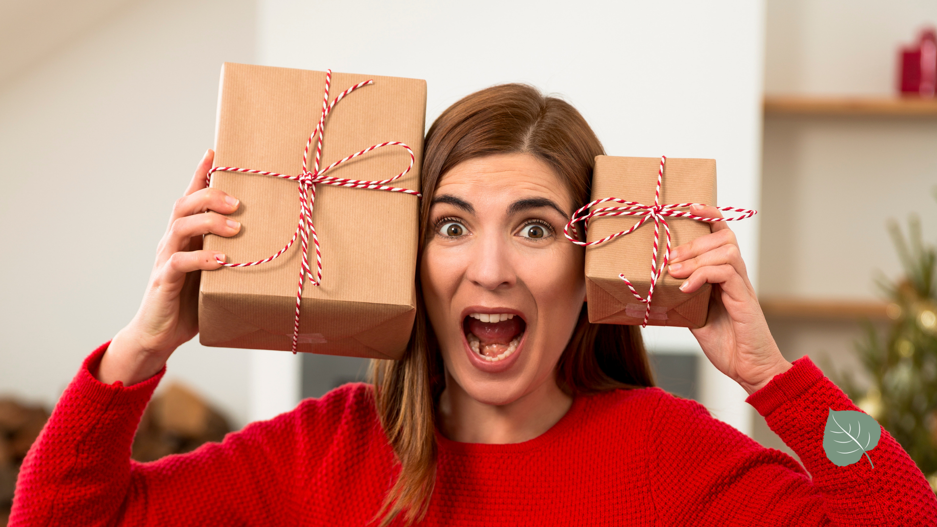 A woman in a red sweater is holding two christmas presents in front of her face.