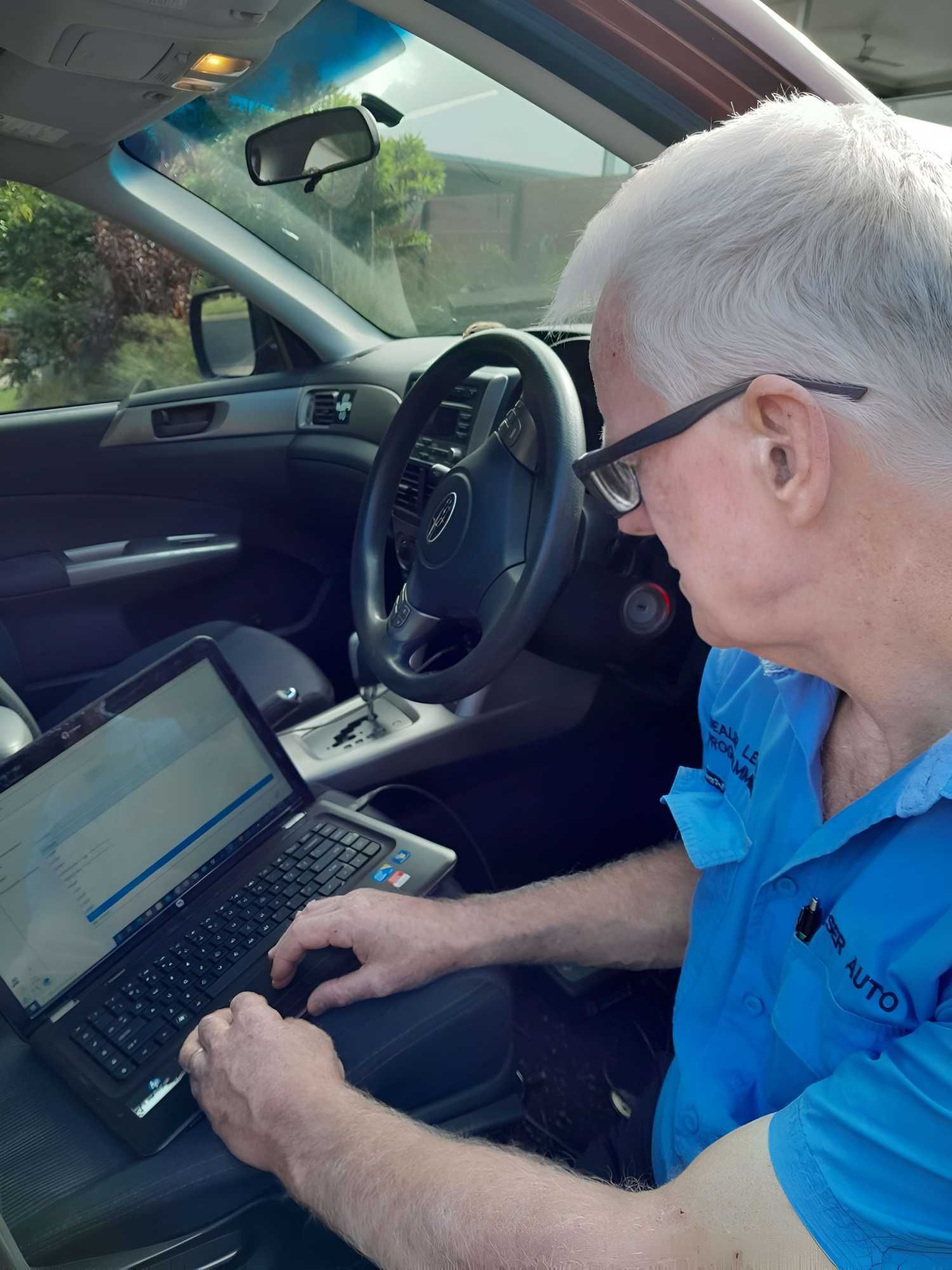 A Man is Sitting in a Car Using a Laptop Computer — Fraser Mobile Auto Tech in Tolga, QLD