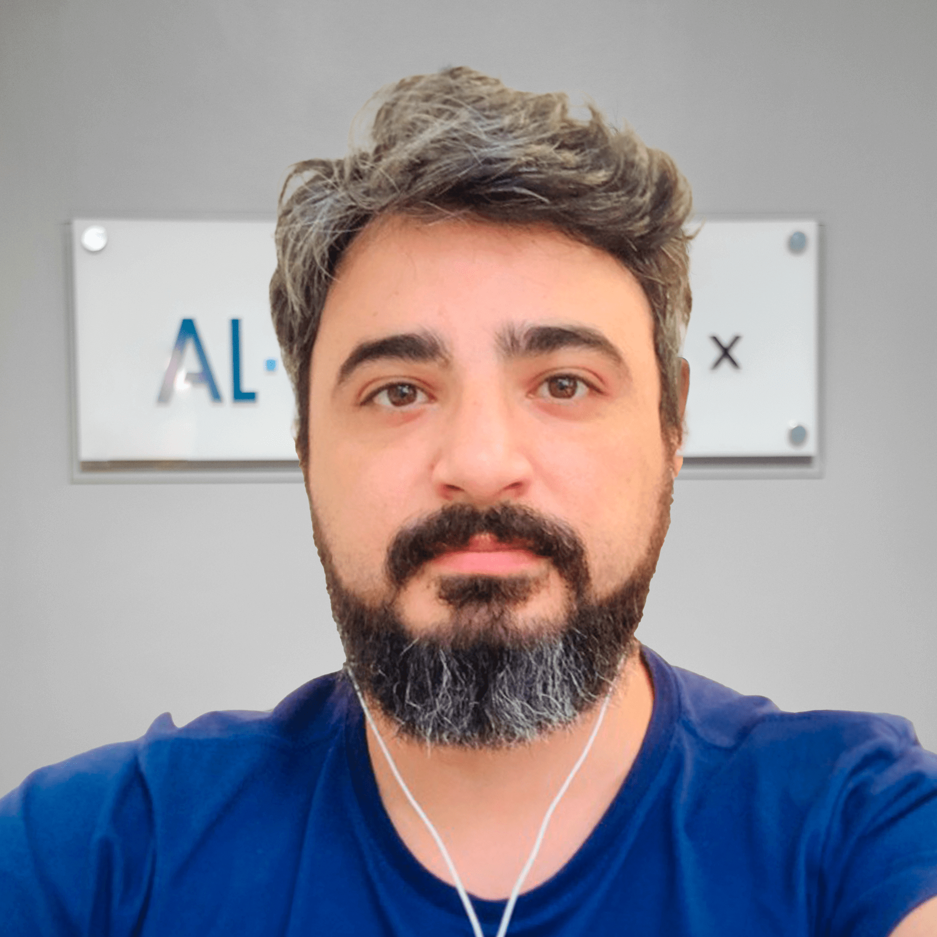 Um homem com barba está usando fones de ouvido em frente a uma placa que diz al