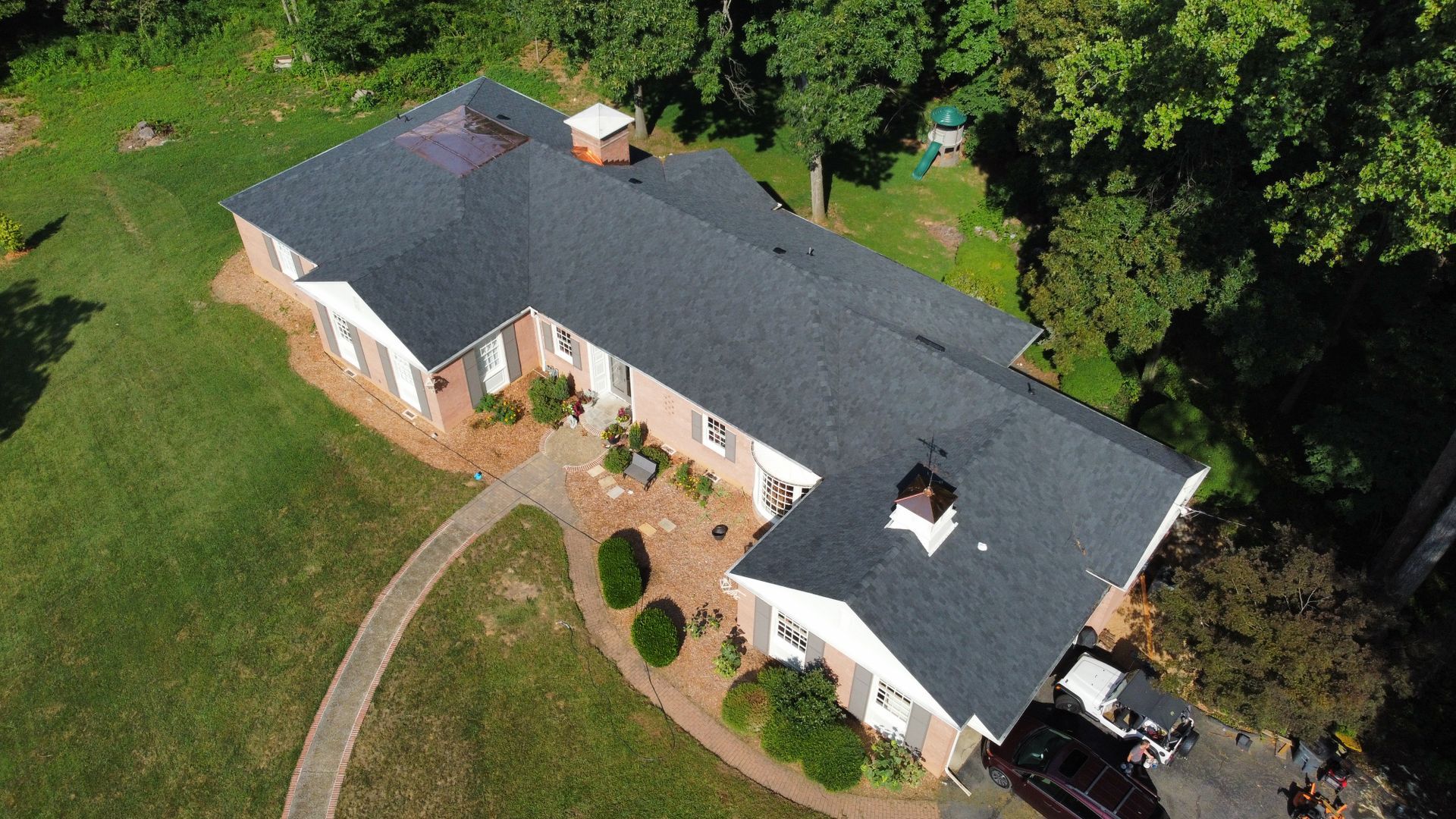 An aerial view of a large brick house with a black roof surrounded by trees.