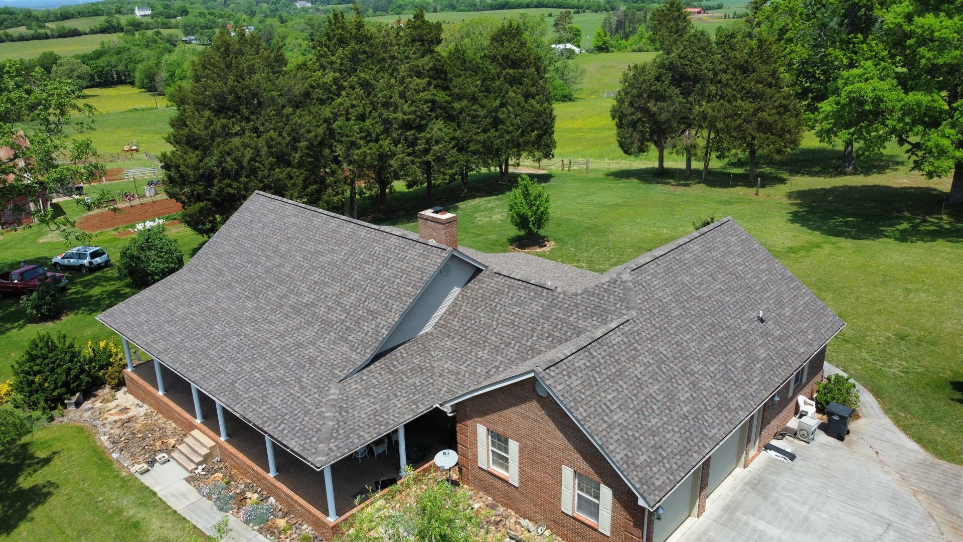 An aerial view of a brick house with a gray roof surrounded by trees and grass.