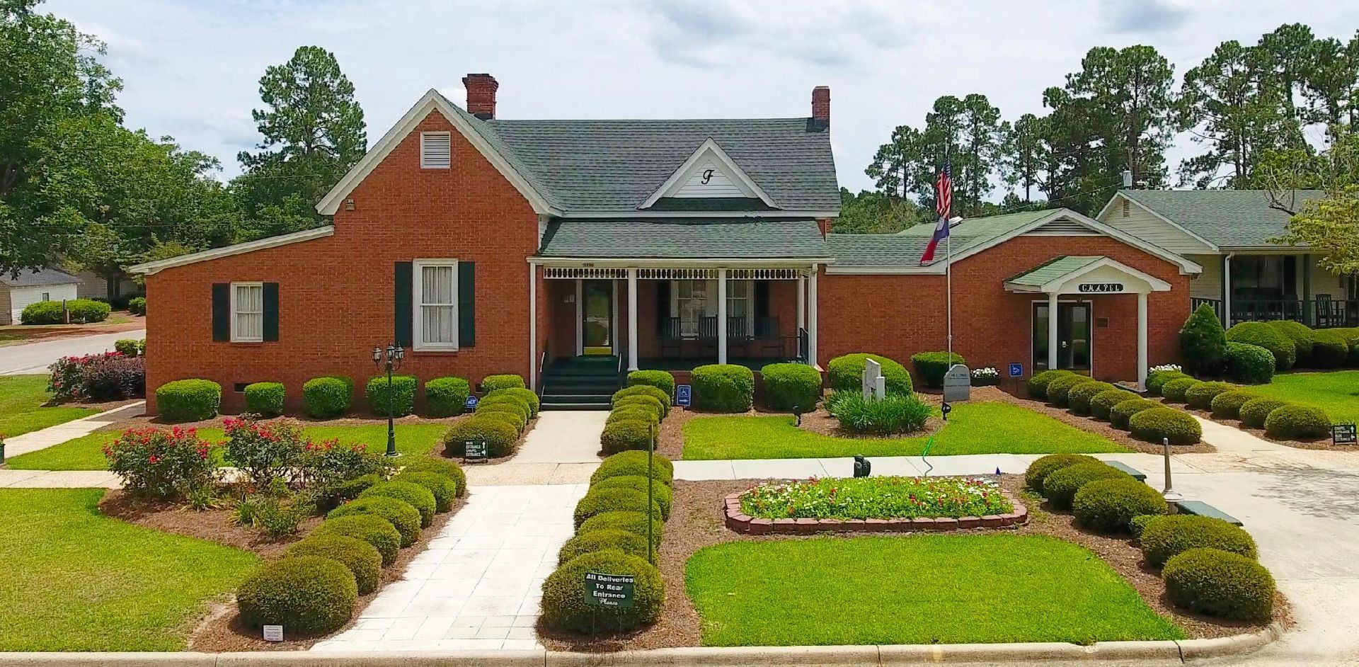 Brick building with a porch, surrounded by green grass and trimmed bushes.