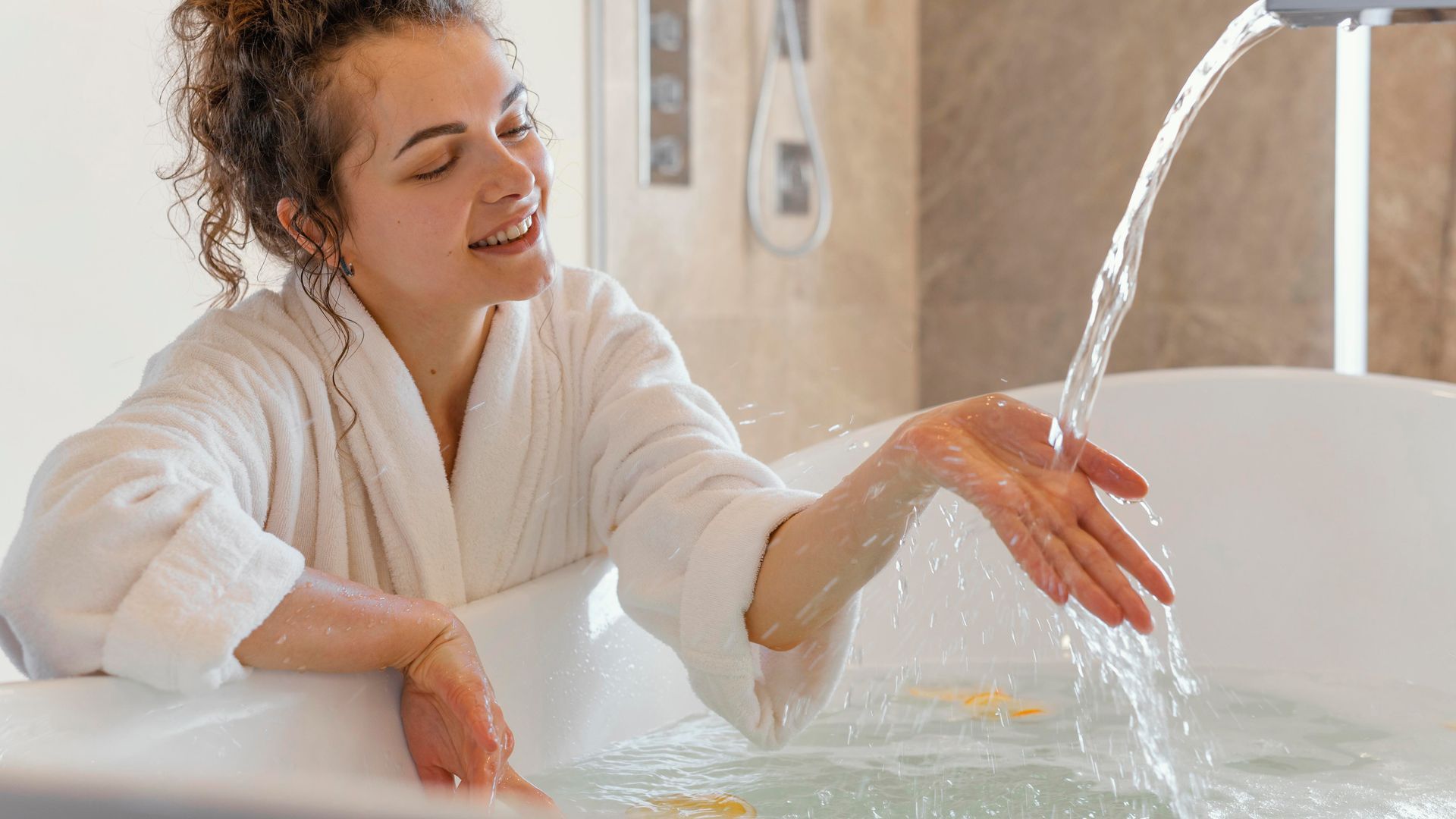 A woman is taking a bath in a bathtub and touching the water.