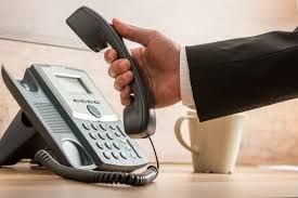 A person is talking on a telephone next to a cup of coffee.