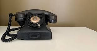 An old black telephone is sitting on a white table.