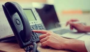 A person is pressing a button on a telephone while using a laptop.