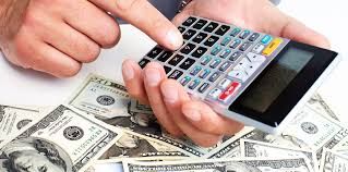 A person is holding a calculator over a pile of money.