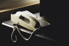 A telephone is sitting on a shelf next to a computer.