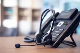 A headset is sitting next to a telephone on a wooden table.
