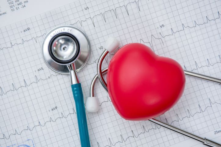 Un cuore rosso è seduto sopra un grafico ECG accanto a uno stetoscopio.