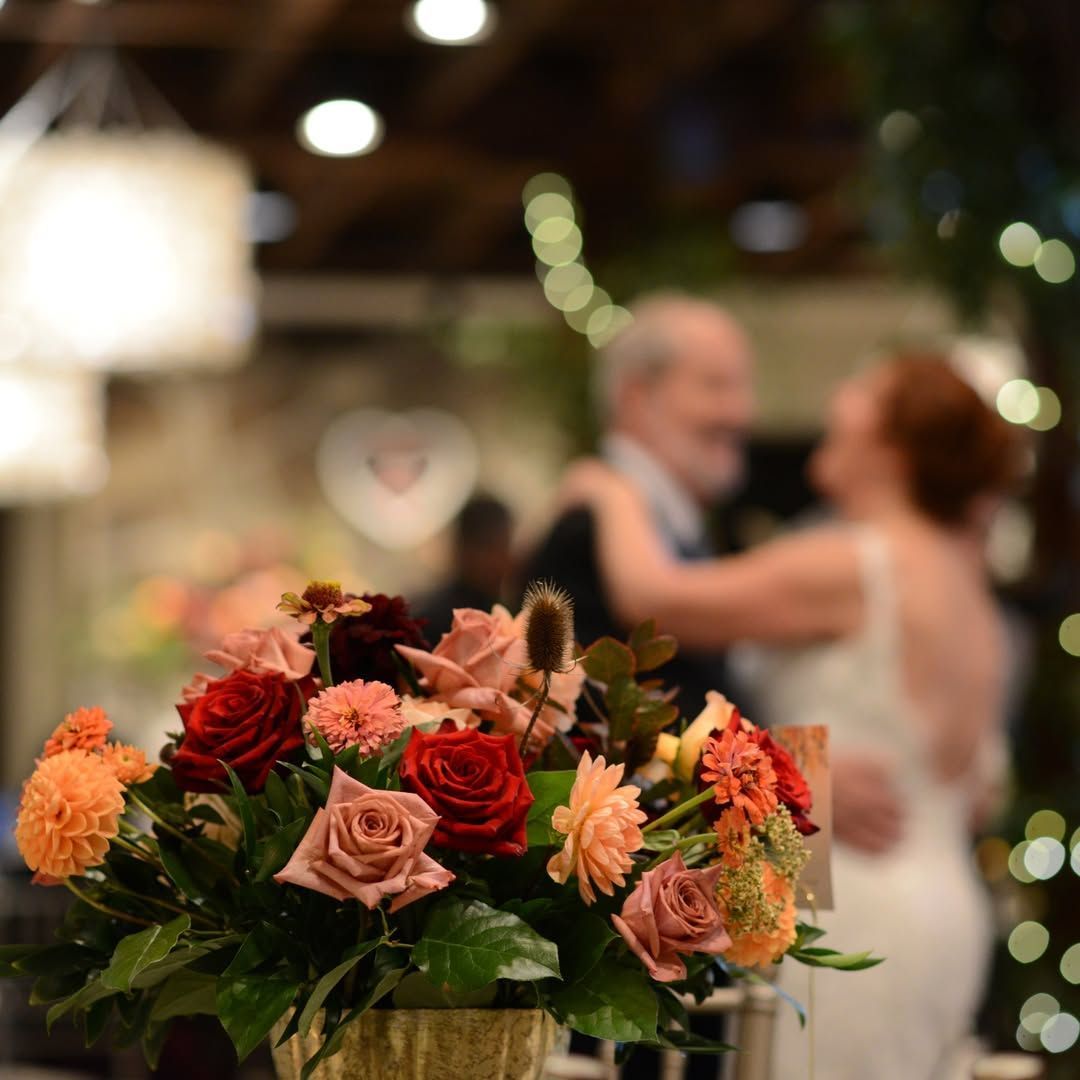 Orange and pink bouquet in foreground at a blurred wedding dance scene