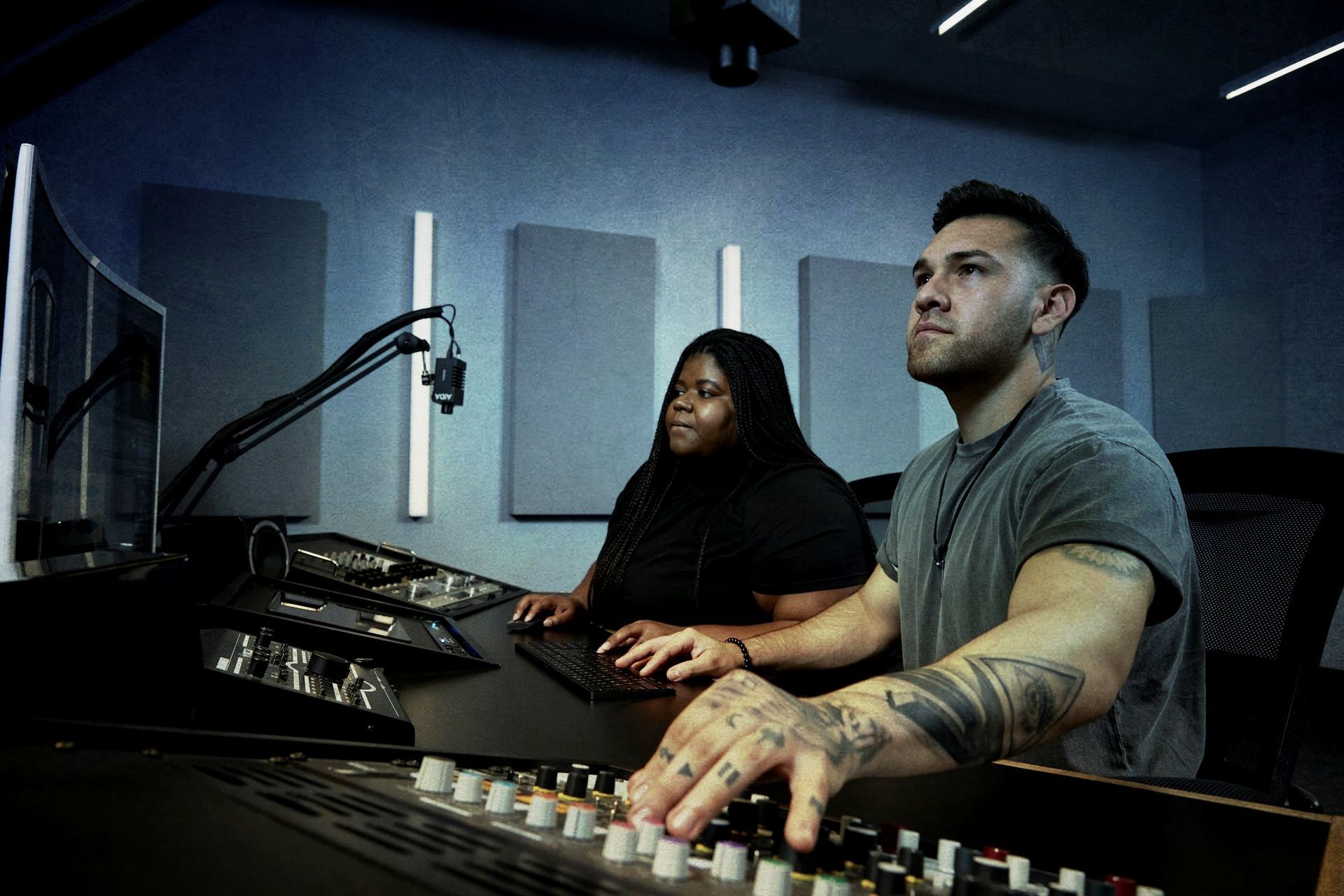 A man and a woman are sitting at a desk in a recording studio.