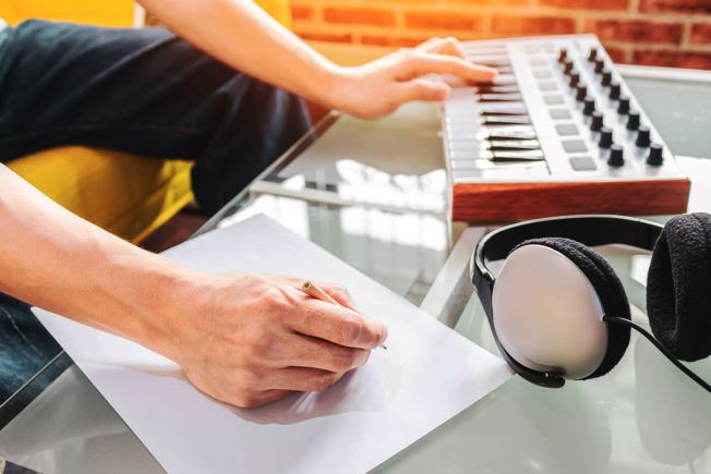 A person is writing on a piece of paper while playing a keyboard.