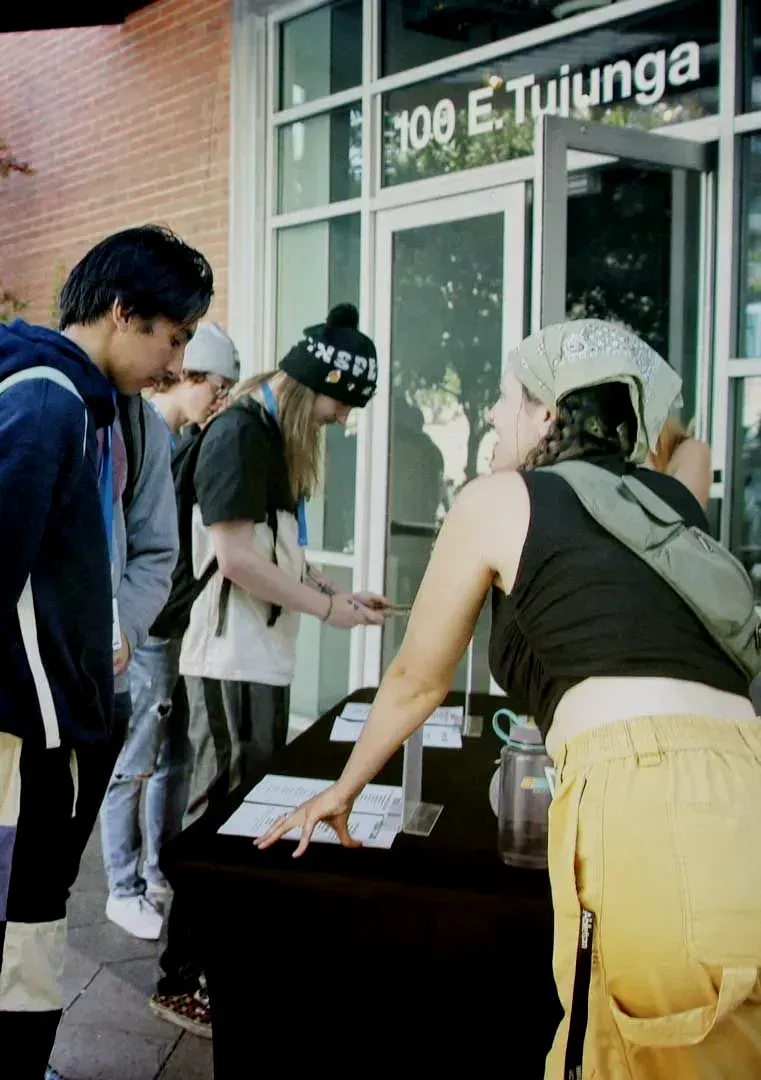 a group of people standing around a table in front of a building that says 100 e tuiunga