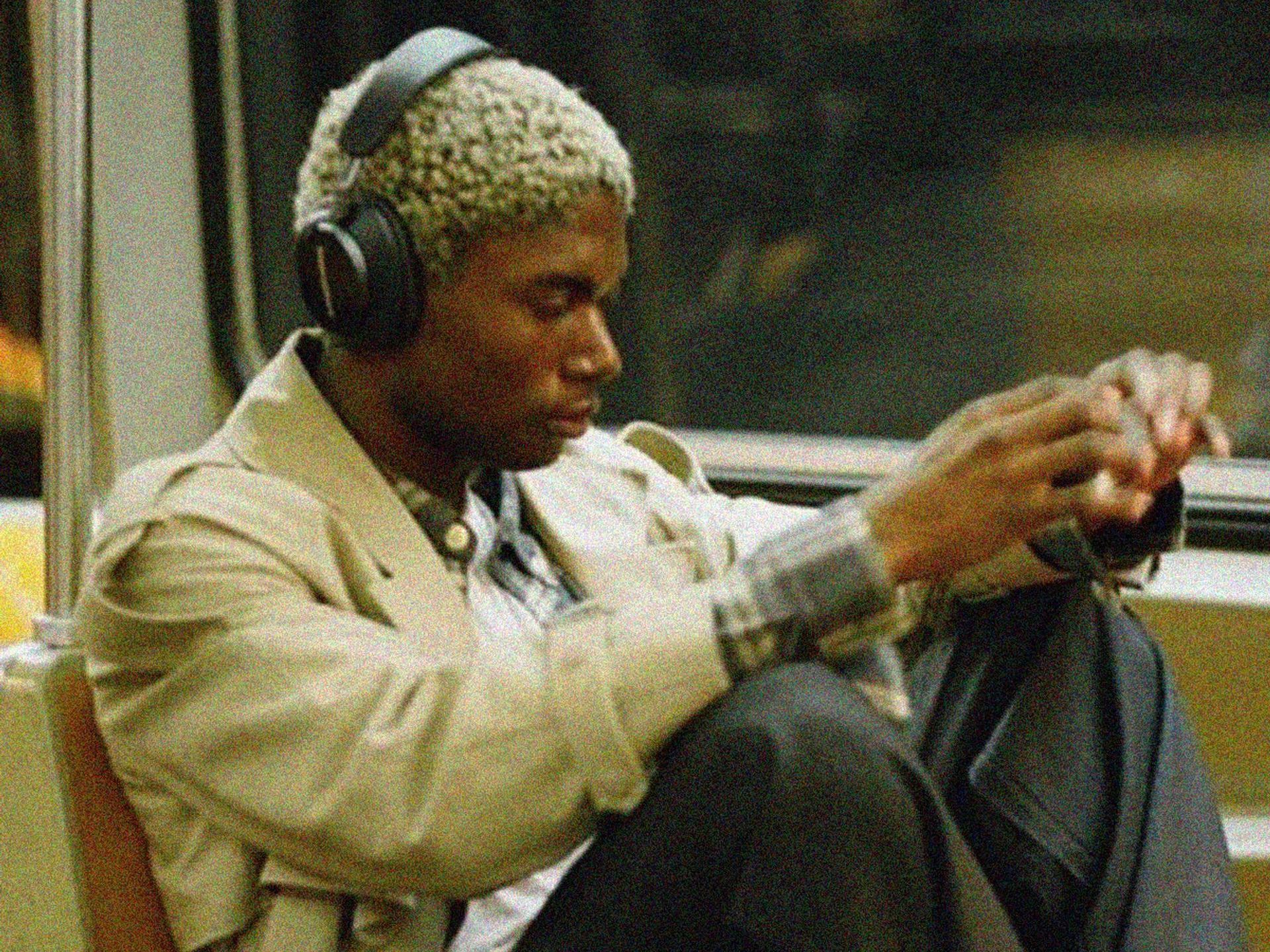 A man wearing headphones is sitting on a bus looking at his phone.