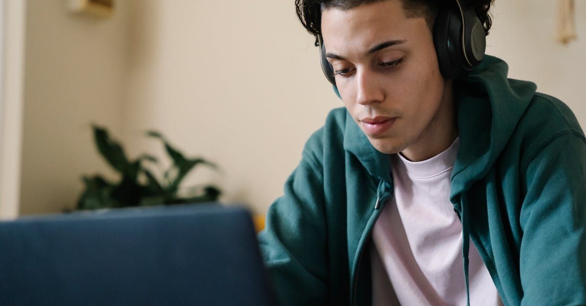 A young music producer wearing headphones is using a laptop computer to produce music.