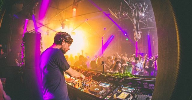 A live electronic music artist performing on stage with vibrant lights and equipment.