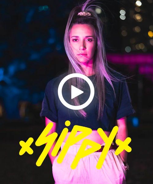 A woman with purple hair is standing in front of a play button