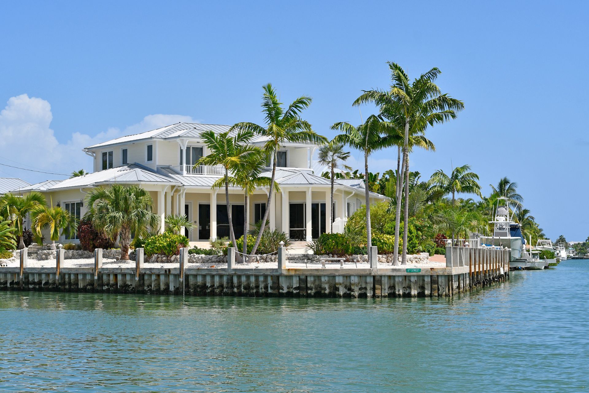 Luxury white house with palm trees on a waterway, blue sky.