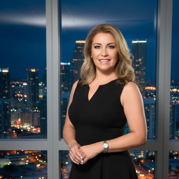 Woman in a black dress smiles in front of a city skyline at night.