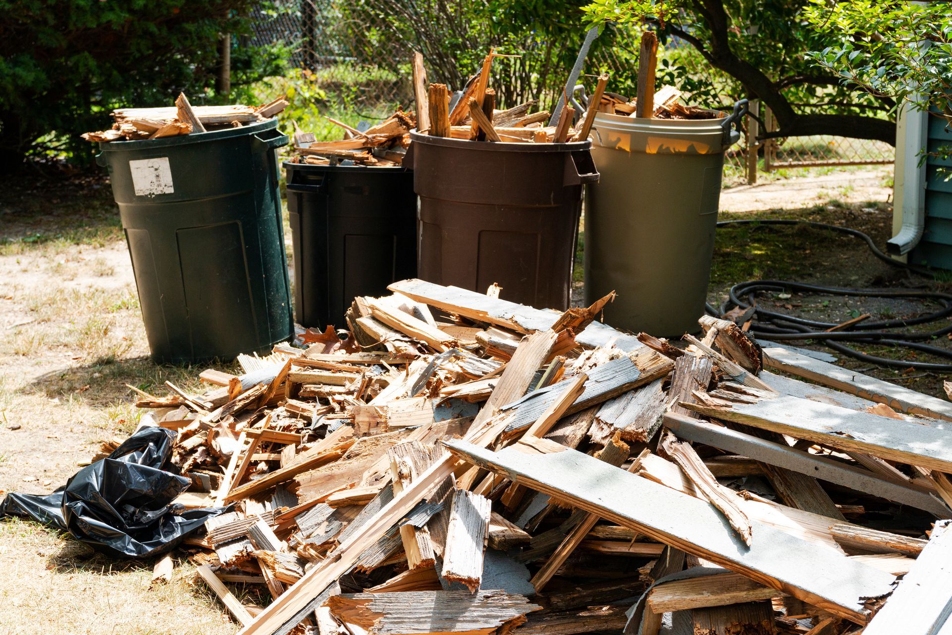 Piles of broken wood and debris beside garbage bins outdoors in a yard or work area