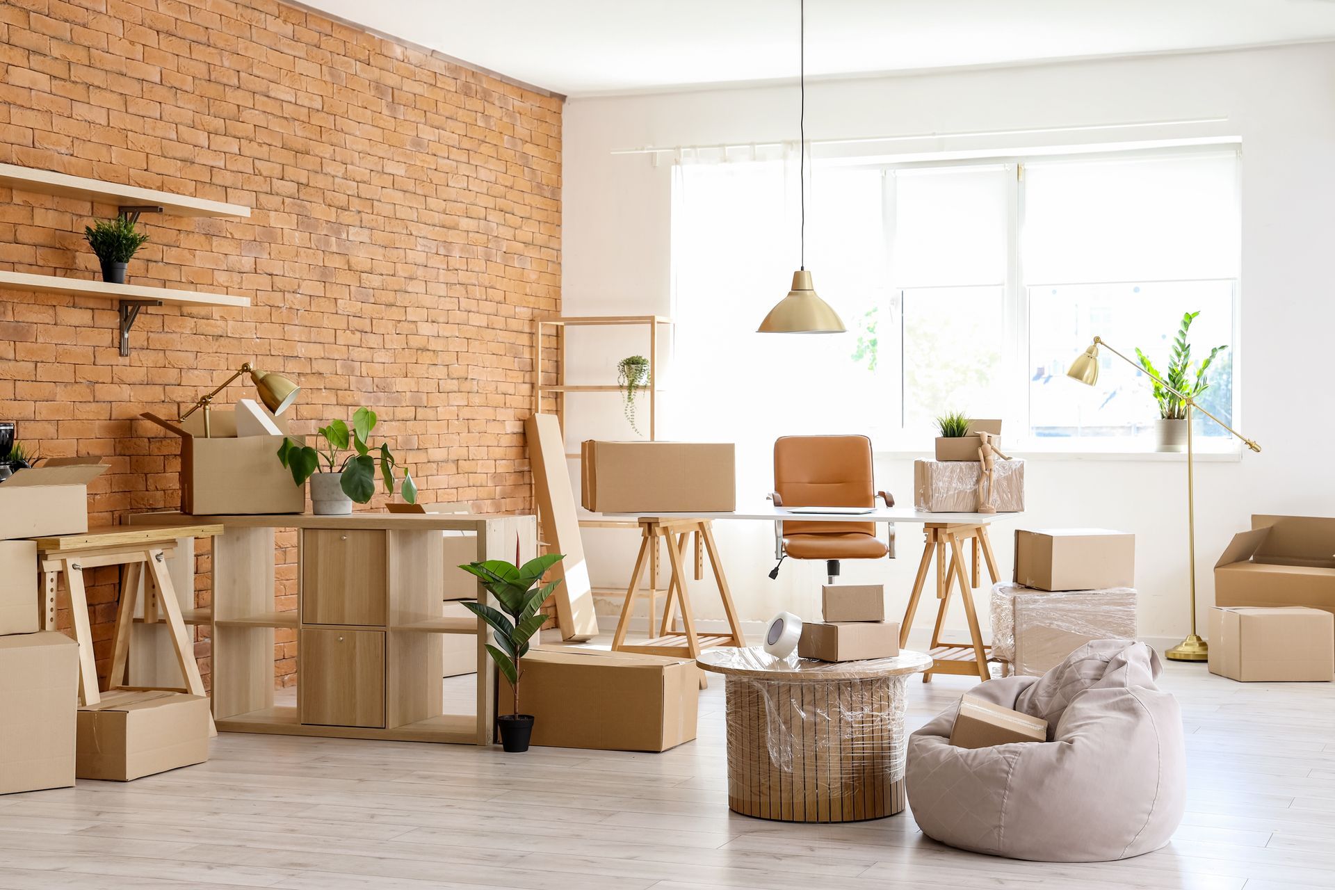 Bright, cozy studio with brick wall, desk, plants, chairs, and a window seat by a large window