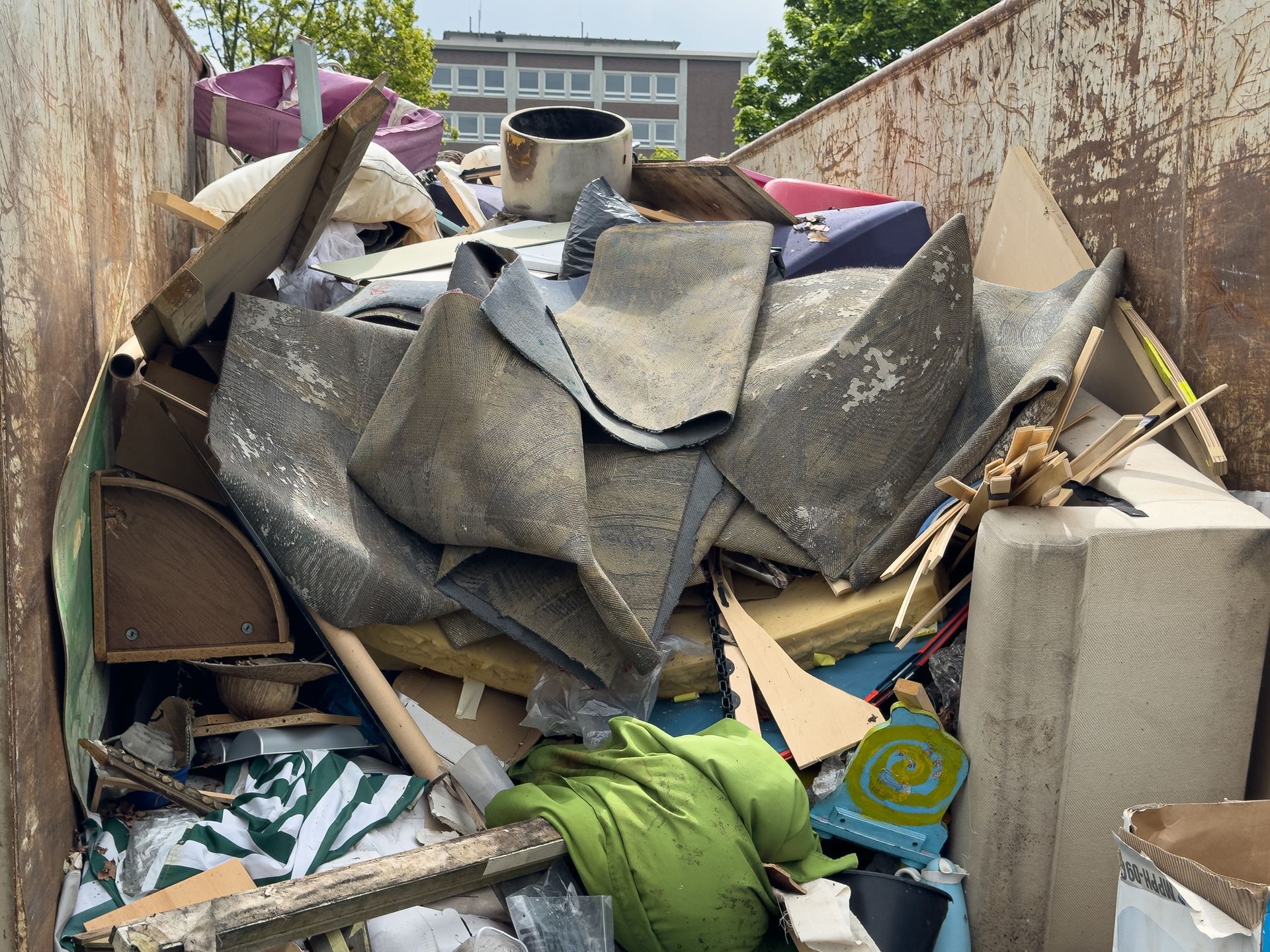 A dump container overflowing with torn carpet, wood scraps, and other construction debris.