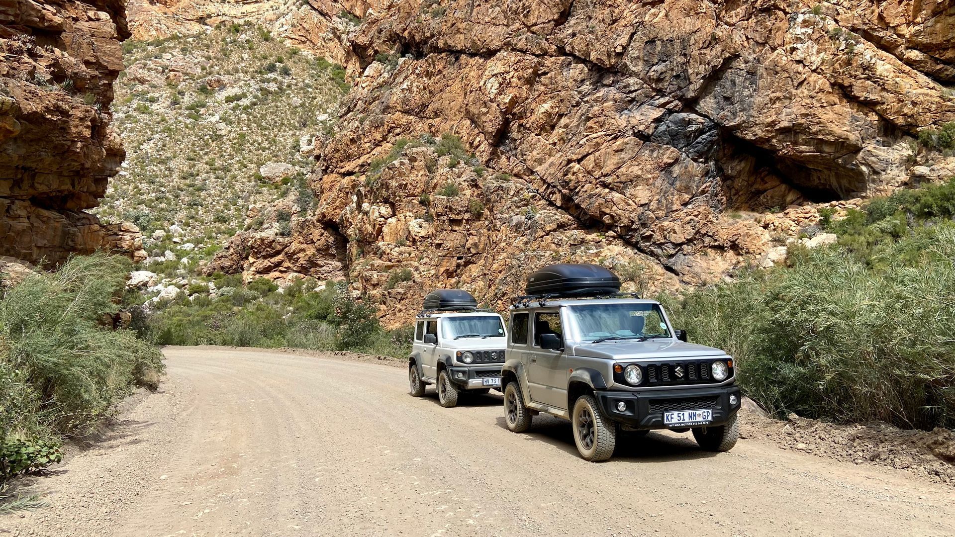 Two SUVs driving on a dirt road through a rocky mountain pass.