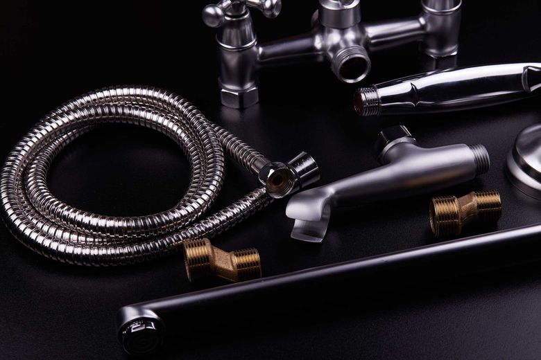 Chrome plumbing fixtures and a shower hose on a black surface.