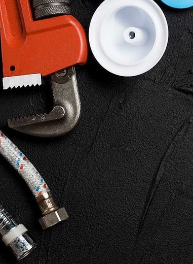 Red pipe wrench, white cap, and braided hose on black textured surface.