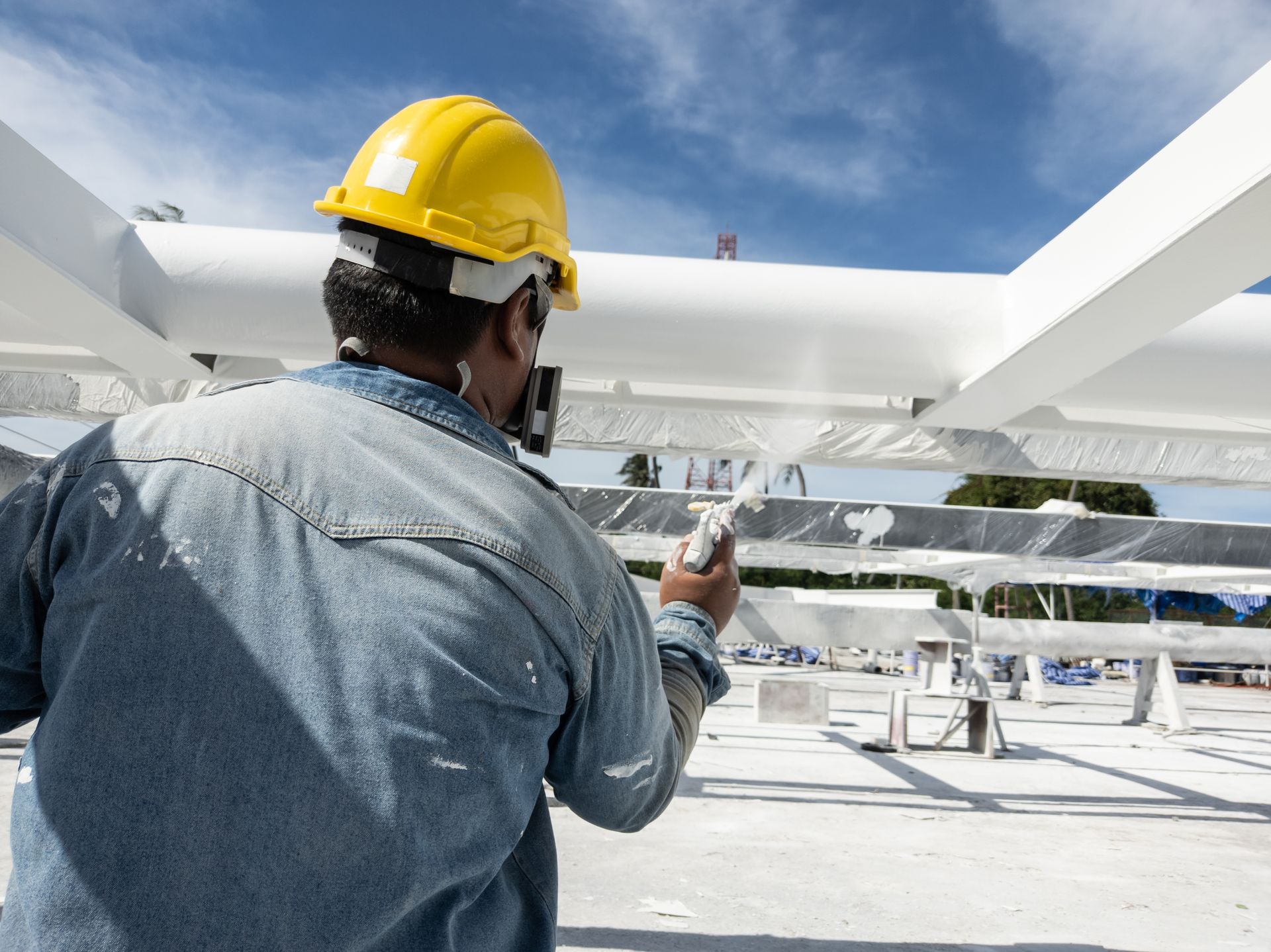 A man wearing a hard hat is painting a metal structure.
