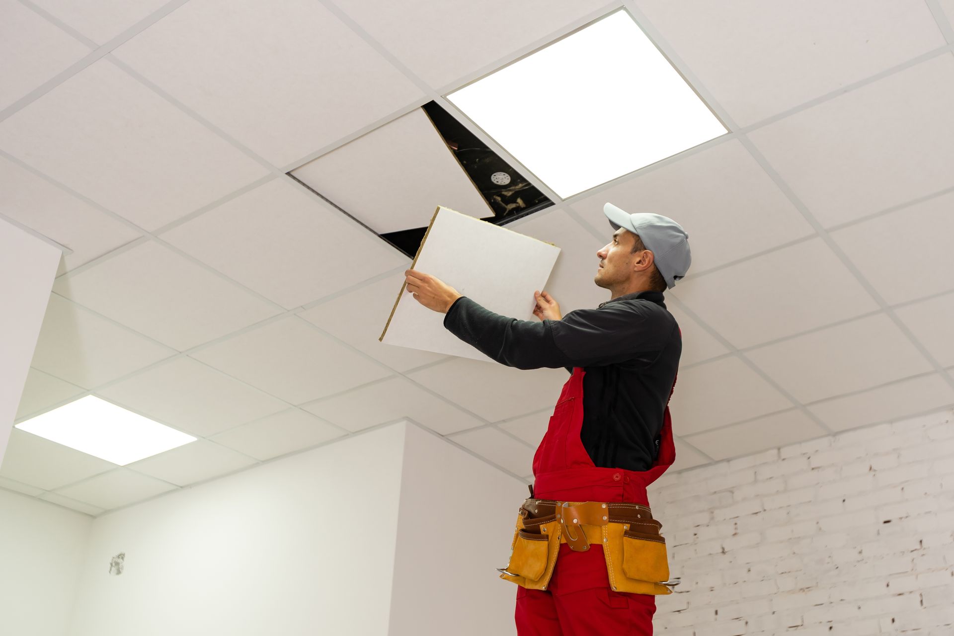 A man is standing on a ceiling holding a piece of paper.