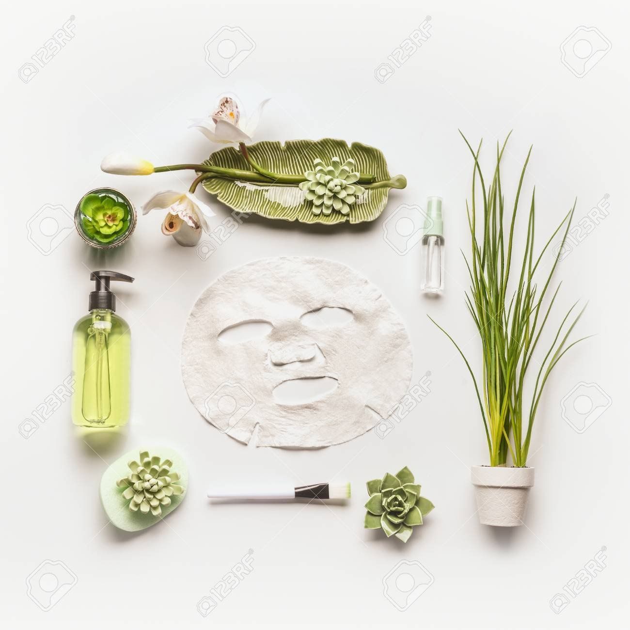 A face mask surrounded by green plants and cosmetics on a white background.