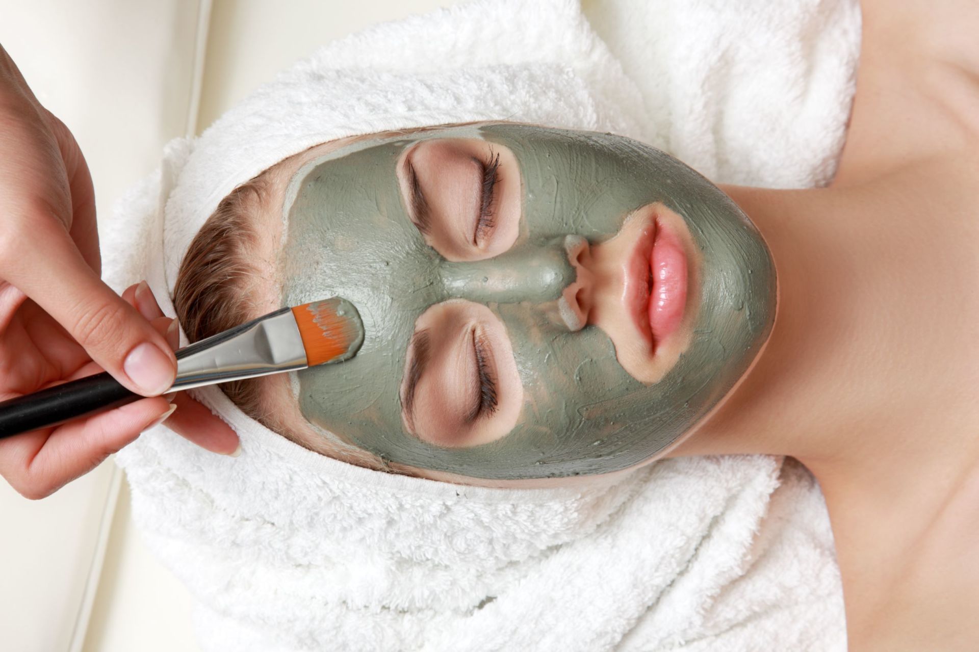 A woman is getting a green clay mask on her face.