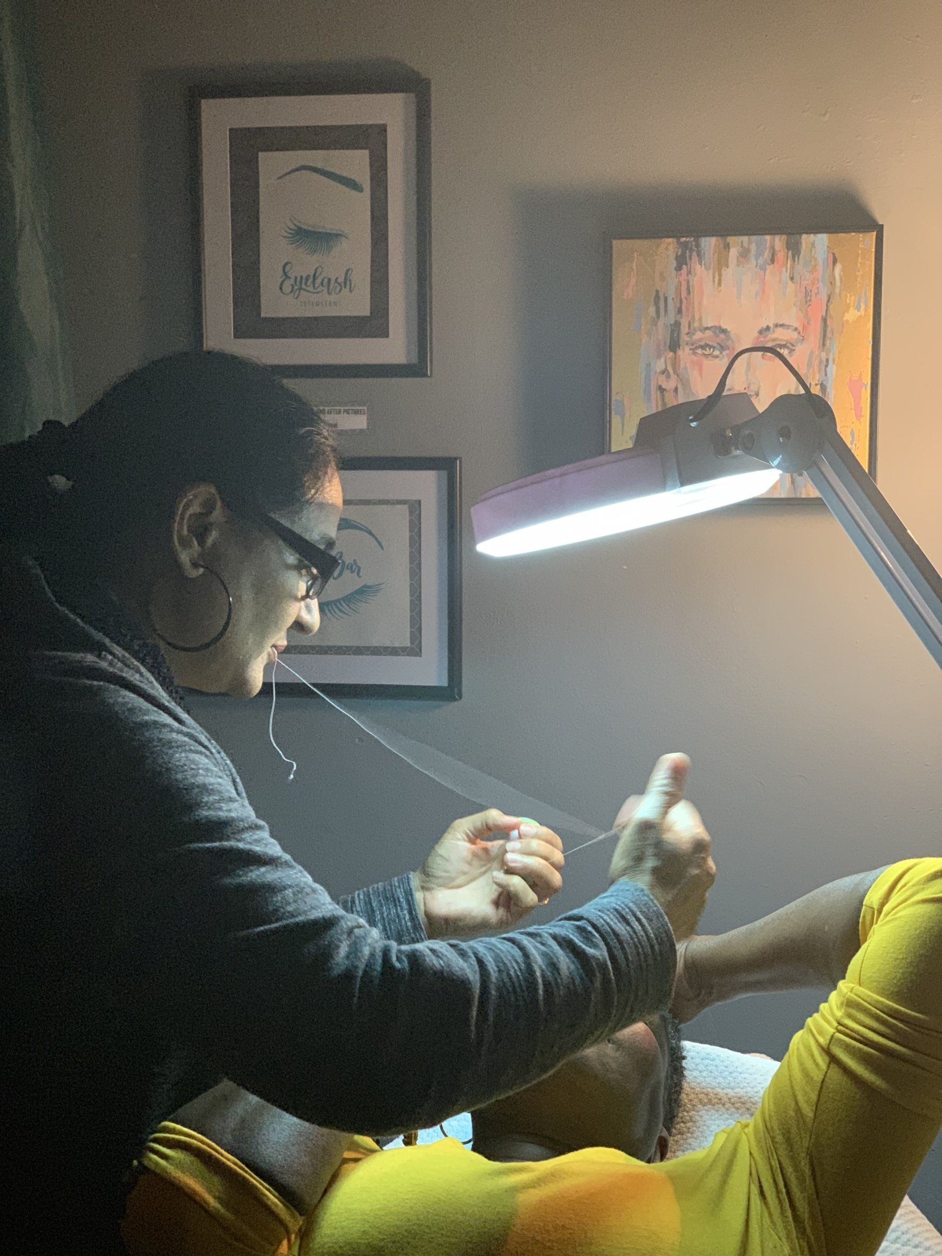 A woman is working on a man 's eyebrows under a lamp.