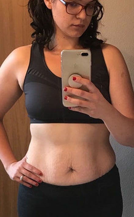 A woman is taking a selfie of her stomach in a mirror.