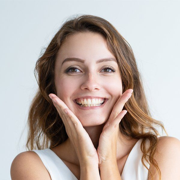 A woman is smiling with her hands on her face.