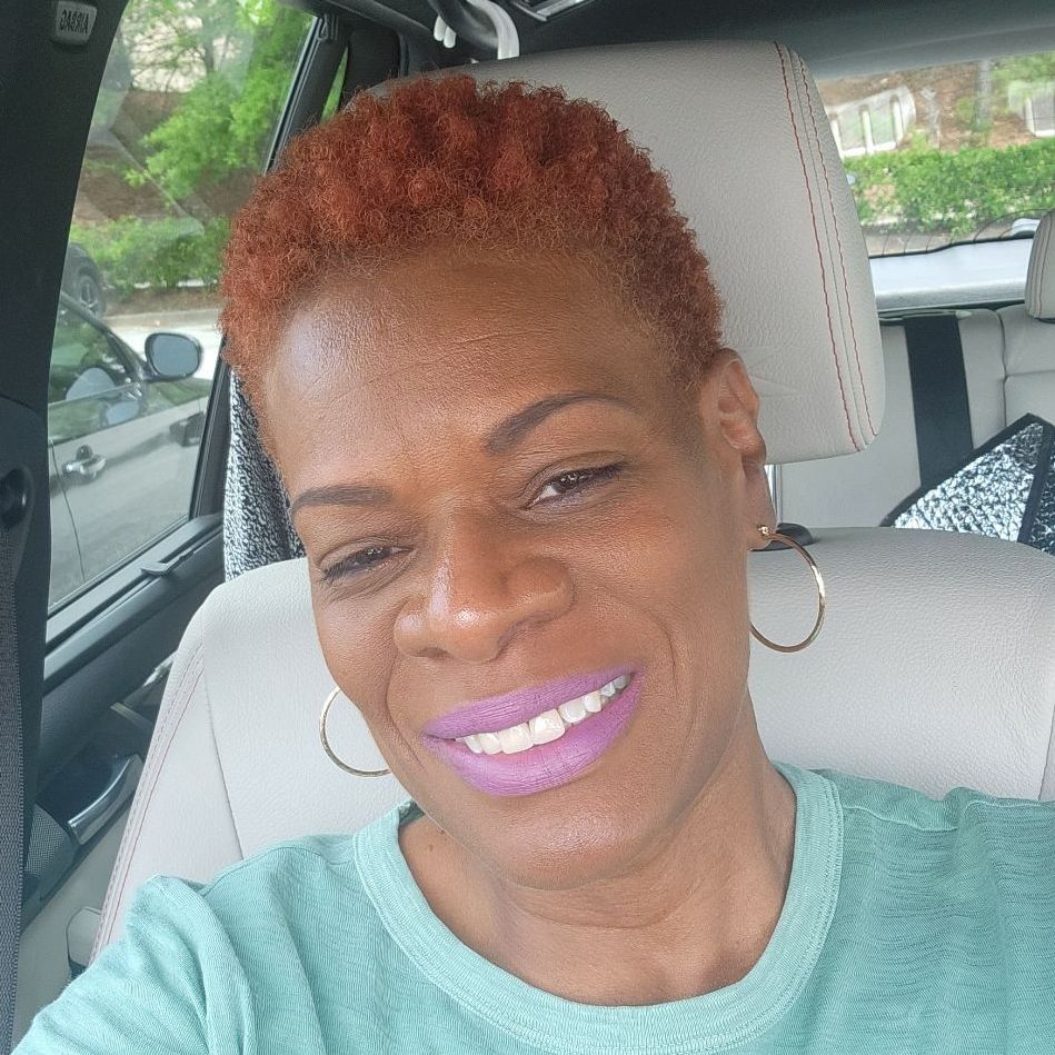 A woman with red hair is smiling while sitting in the back seat of a car.