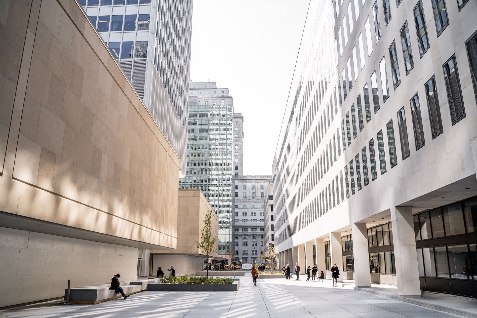 Modern city plaza with tall office buildings, pedestrians, and bright sunlight