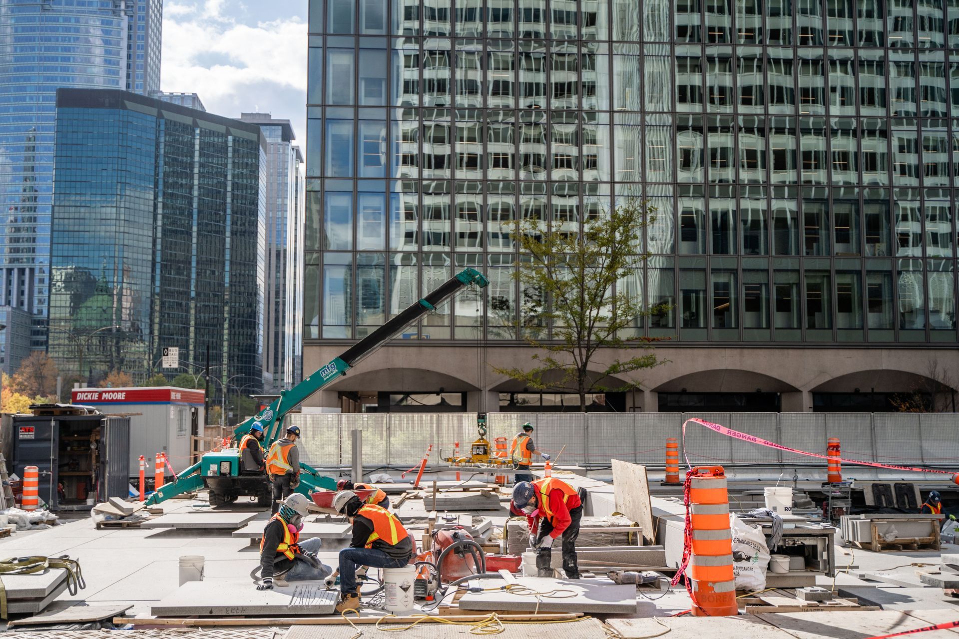 Construction site with workers in safety vests, crane, and modern buildings in background.
