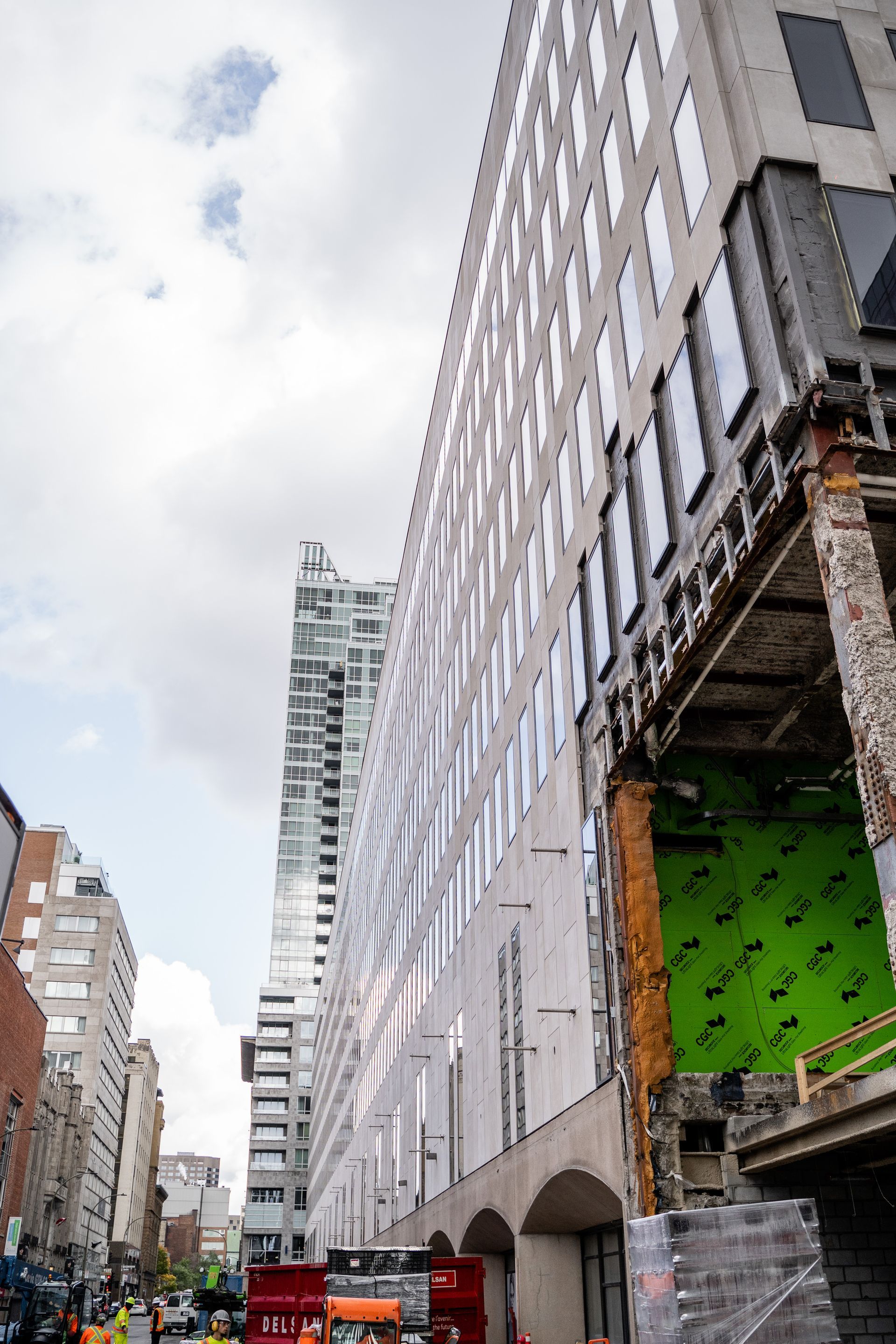 Building under construction with tall white structure, brick building, cloudy sky.