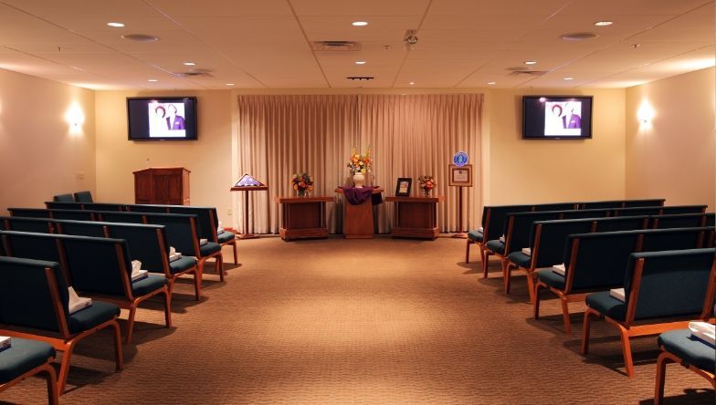 a funeral home with rows of green chairs and a television on the wall .