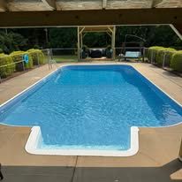 Swimming pool with blue water surrounded by concrete, under a wooden roof.