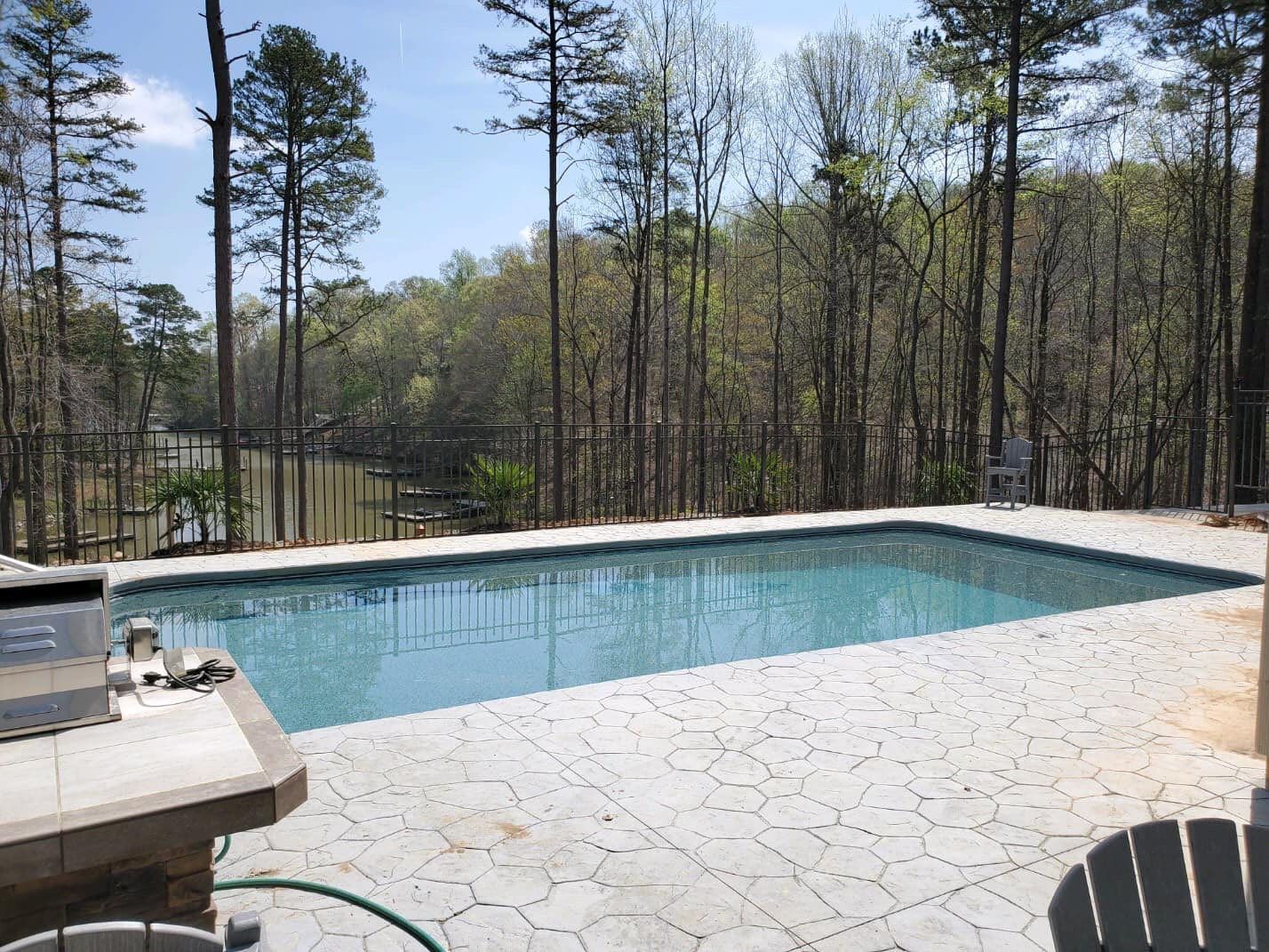 Pool surrounded by patio, with a view of trees and a waterway.