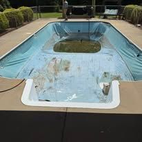 Swimming pool covered in blue tarp, dirty with debris, empty, and outdoors.