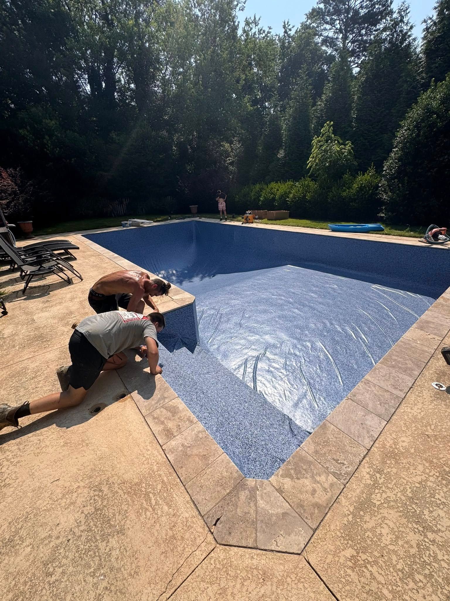 Two people working on the edge of a blue-tiled swimming pool. Outdoors, sunny day.