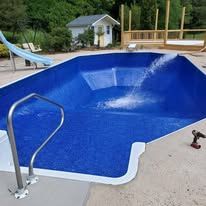 Blue empty swimming pool with a metal ladder and a water fountain.