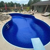 Blue-tiled swimming pool with a diving board; a house is in the background.