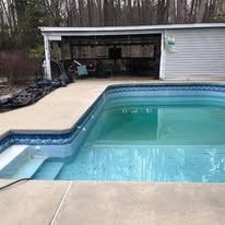 Pool with blue water and steps, next to a concrete patio and a shed.
